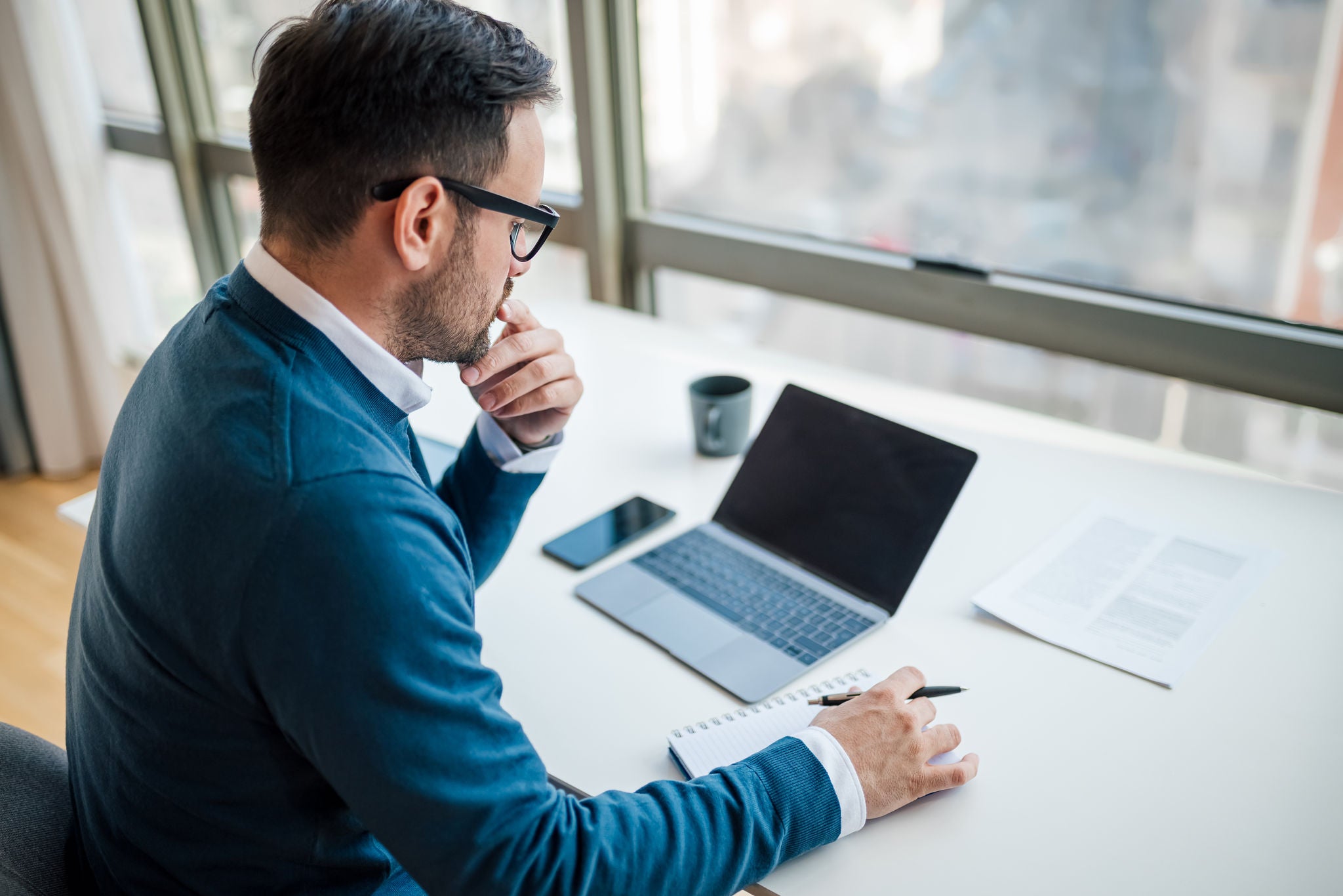 High angle view of serious businessman writing notes in diary. Male executive is using laptop while working at desk. Black blank clean empty mock up template background computer laptop screen.