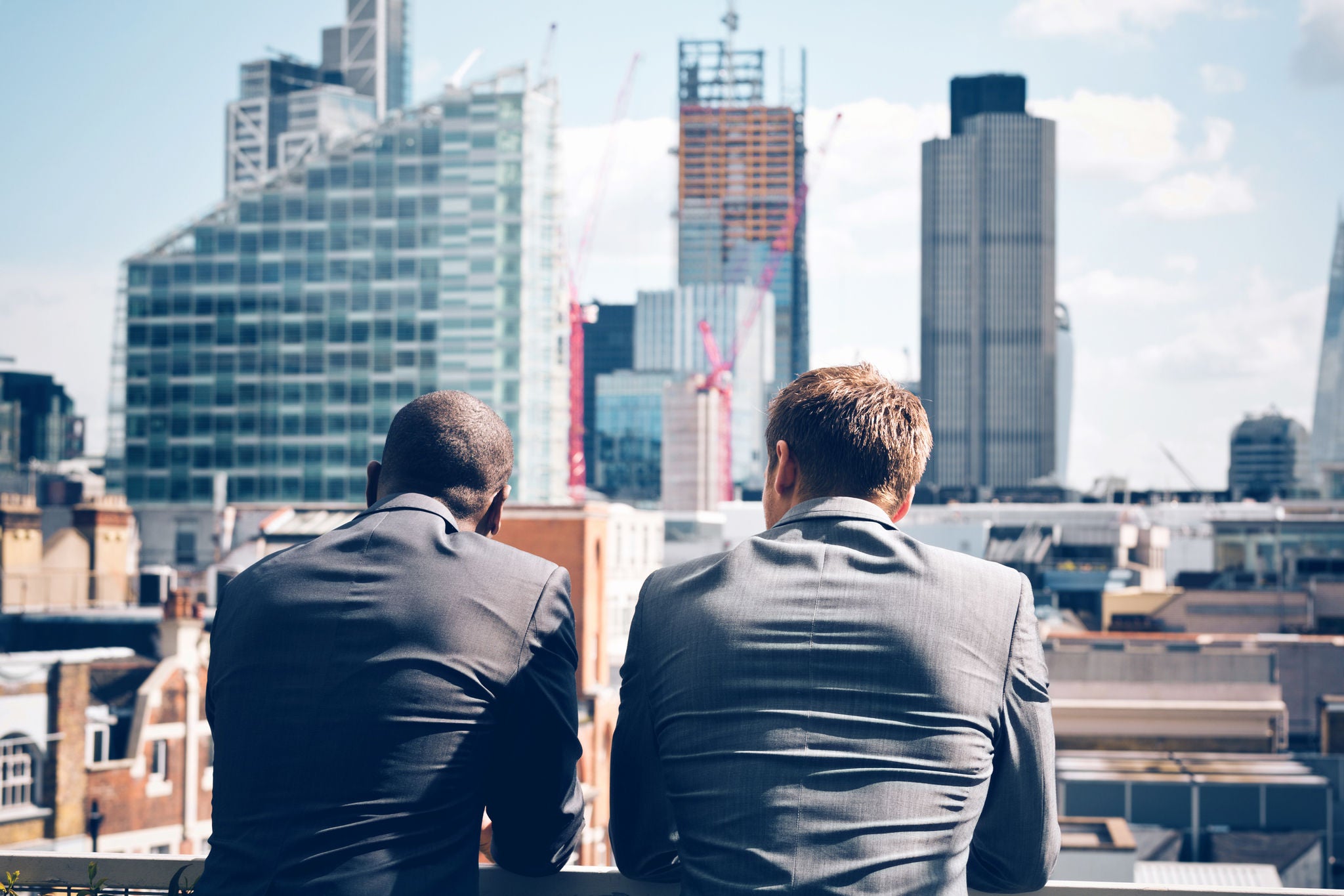 Back view of two businessmen - caucasian and afro american - standing outdoor and looking at city scape.