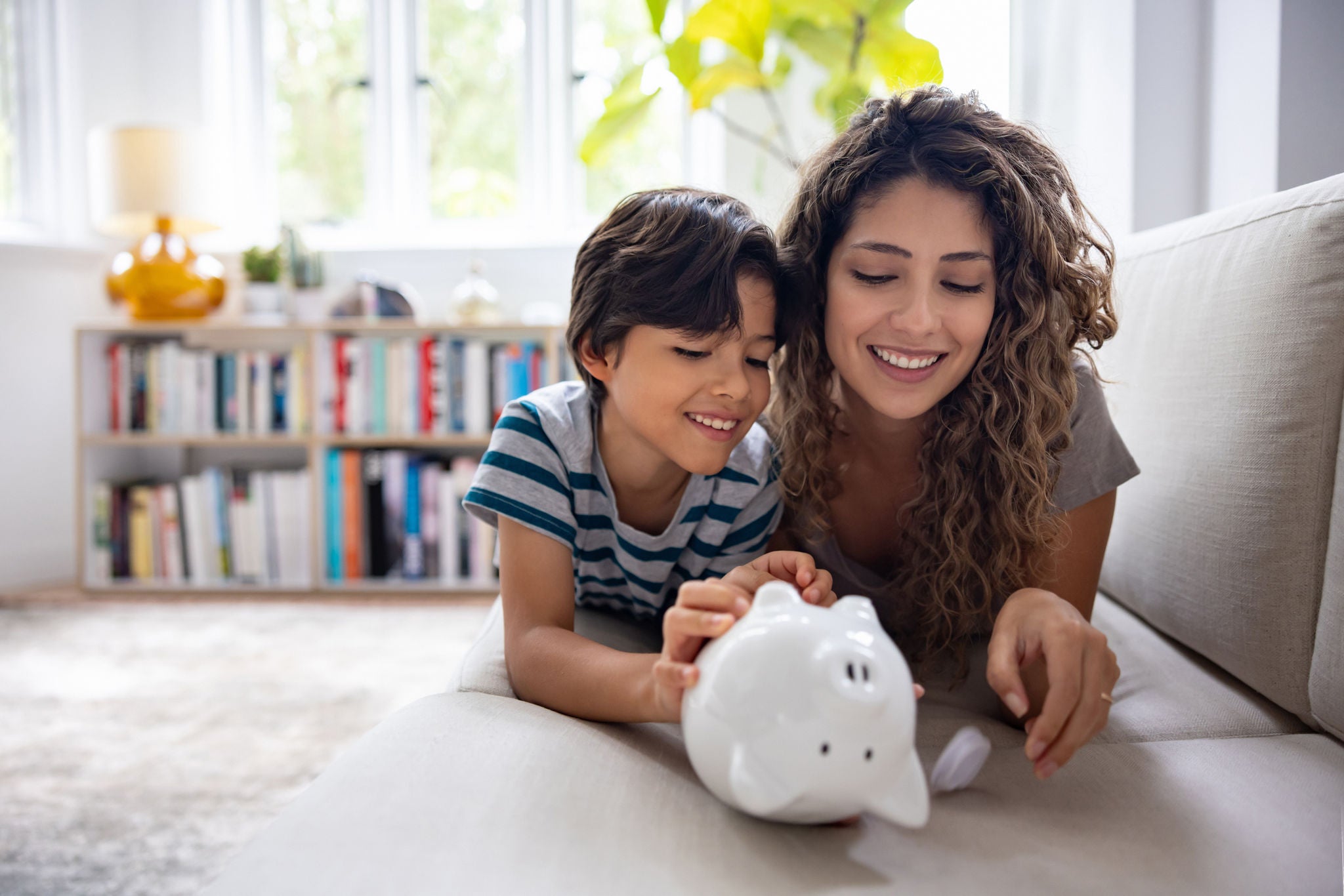 Happy Latin American mother and son braking their piggybank and taking out their savings