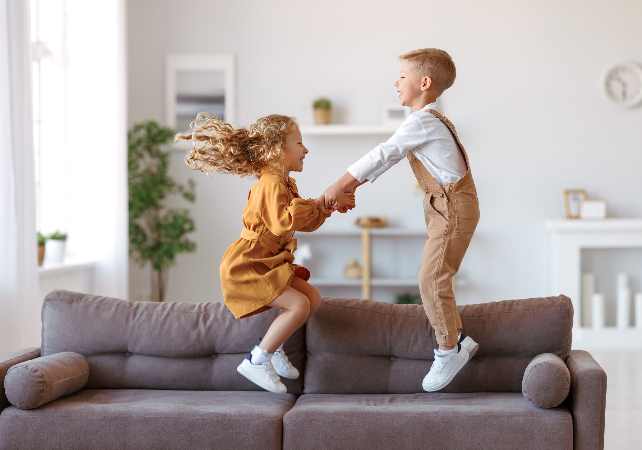 Full length of overjoyed little children brother and sister jumping on sofa, laughing and having fun while playing together at home, kids enjoying carefree leisure time at home